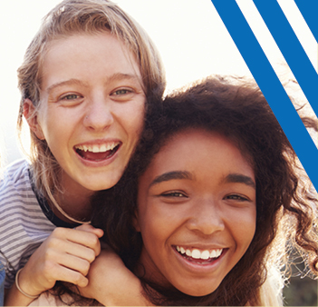 caucasian girl hugging black girl smiling, sunlight